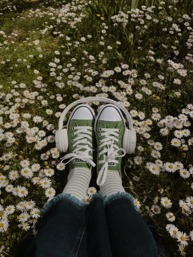 Green sneakers and wireless headphones among chamomile blooms in a meadow.