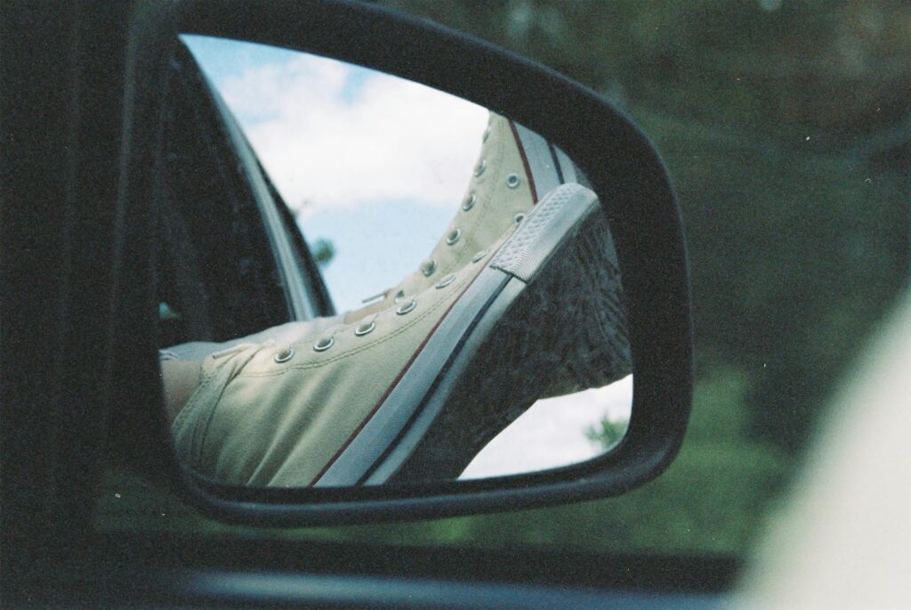 A close-up view of sneakers reflected in a car's side mirror, creating a unique travel perspective.