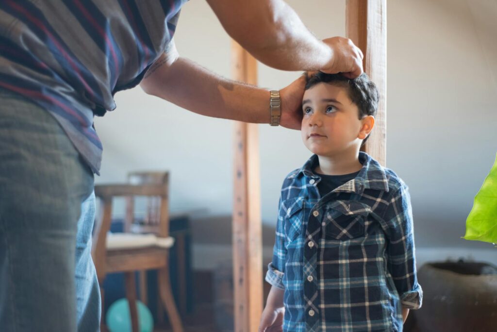 A father marking his young son's height on a wooden pole indoors, capturing a family bonding moment.