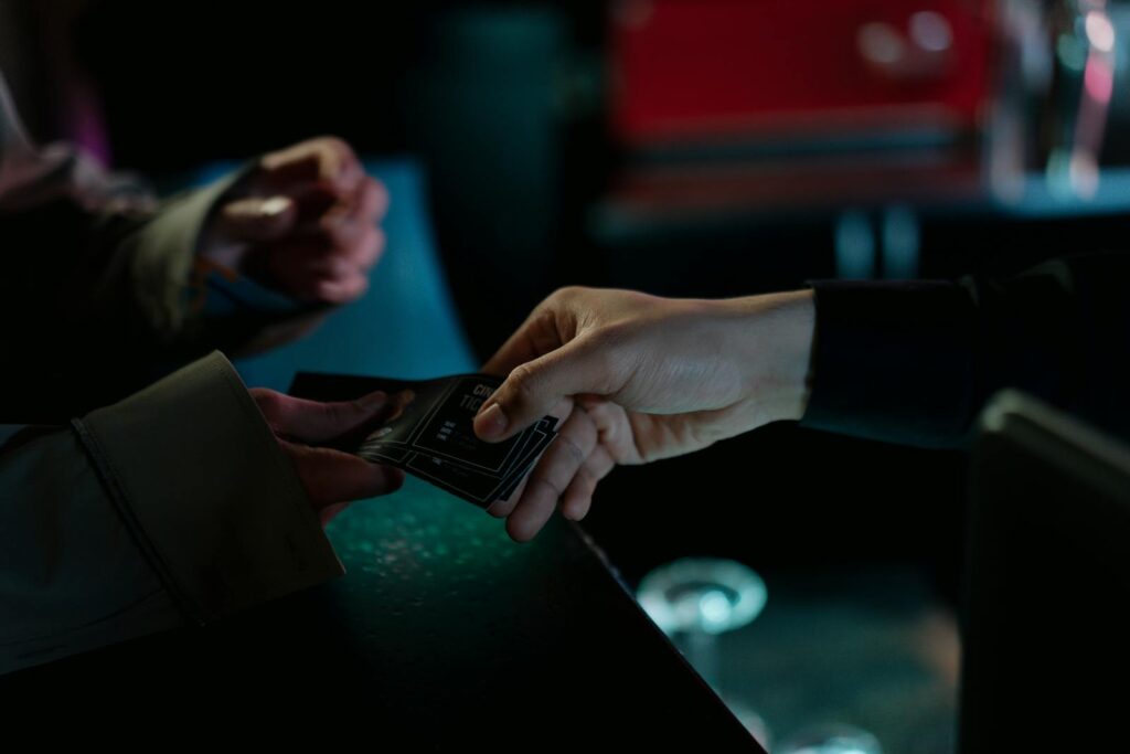 Hands exchanging movie theater tickets indoors, capturing a cinematic moment.