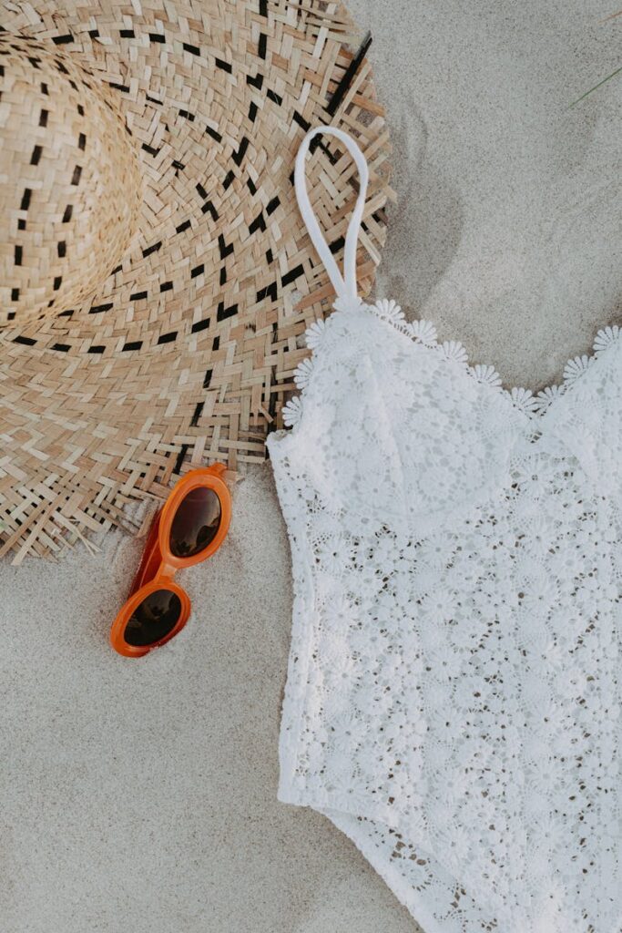 A laid-back summer vibe with a straw hat, lace swimsuit, and sunglasses on sandy beach.
