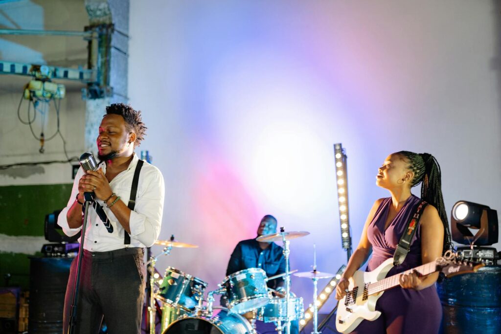 Vibrant indoor musical performance featuring a band with a singer, drummer, and guitarist under colorful spotlights.