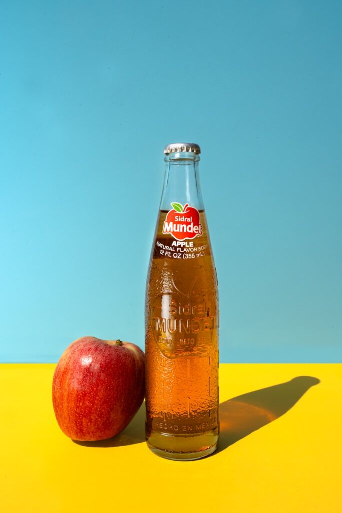 A bottle of apple cider next to an apple