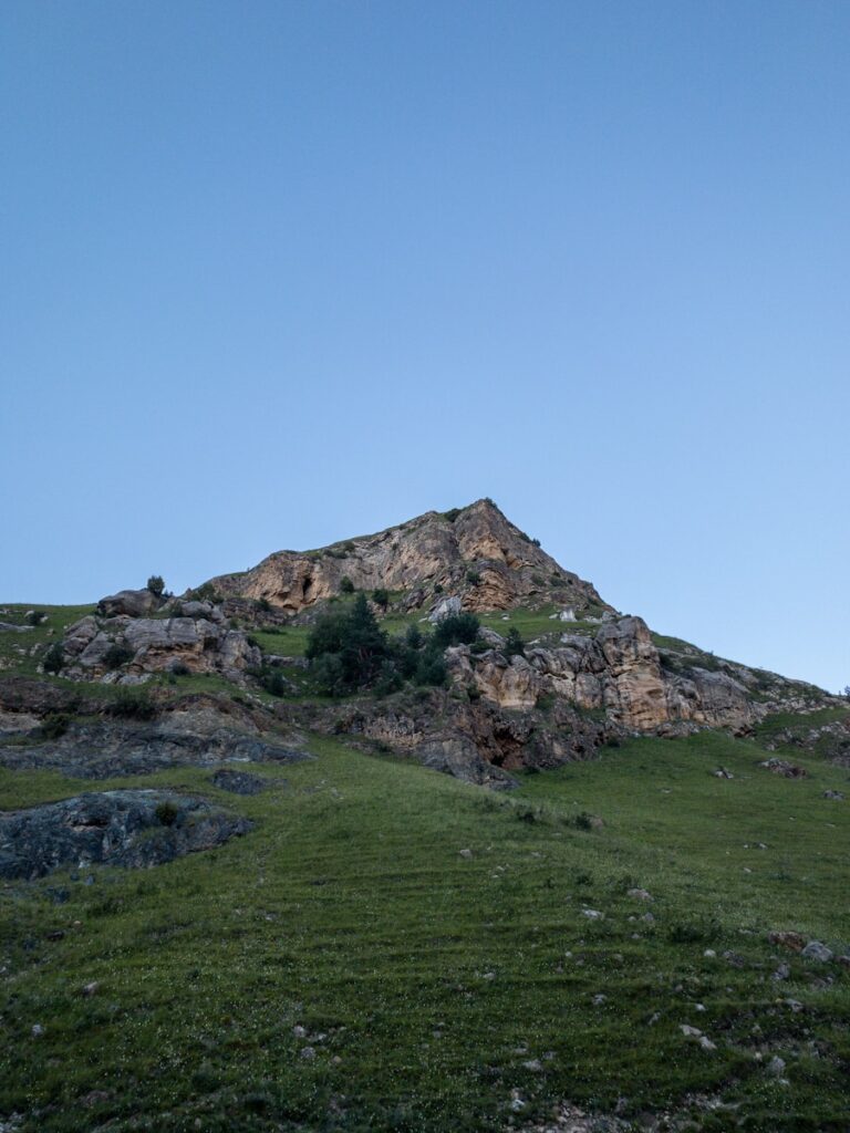 green grass field near mountain under blue sky during daytime