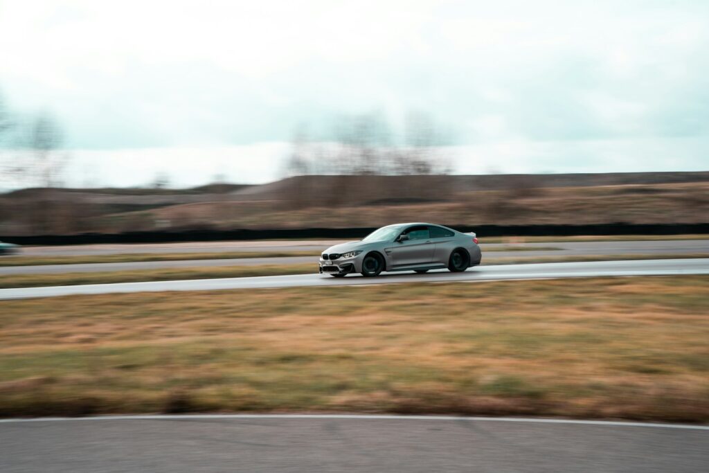 a silver car driving down a road next to a lush green field
