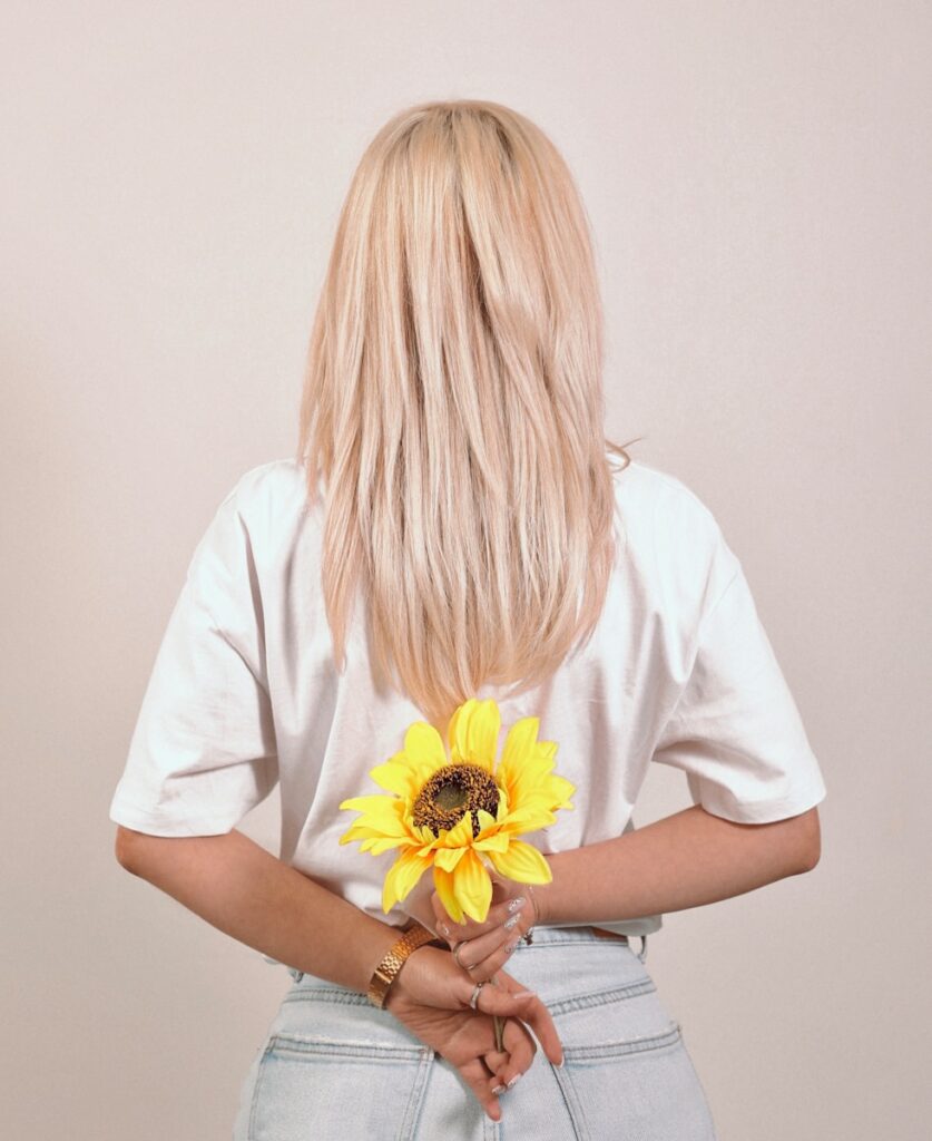 a woman with blonde hair holding a sunflower