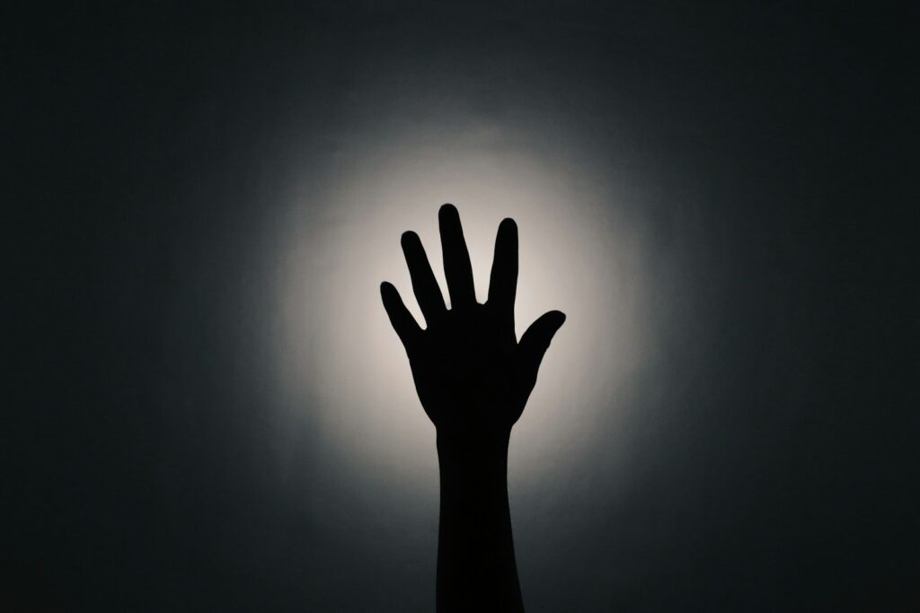 a silhouette of a hand reaching up towards the sun