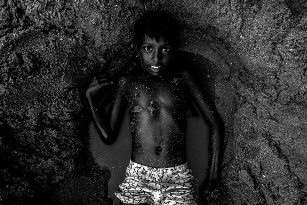 grayscale photography of topless boy lying on wet sand