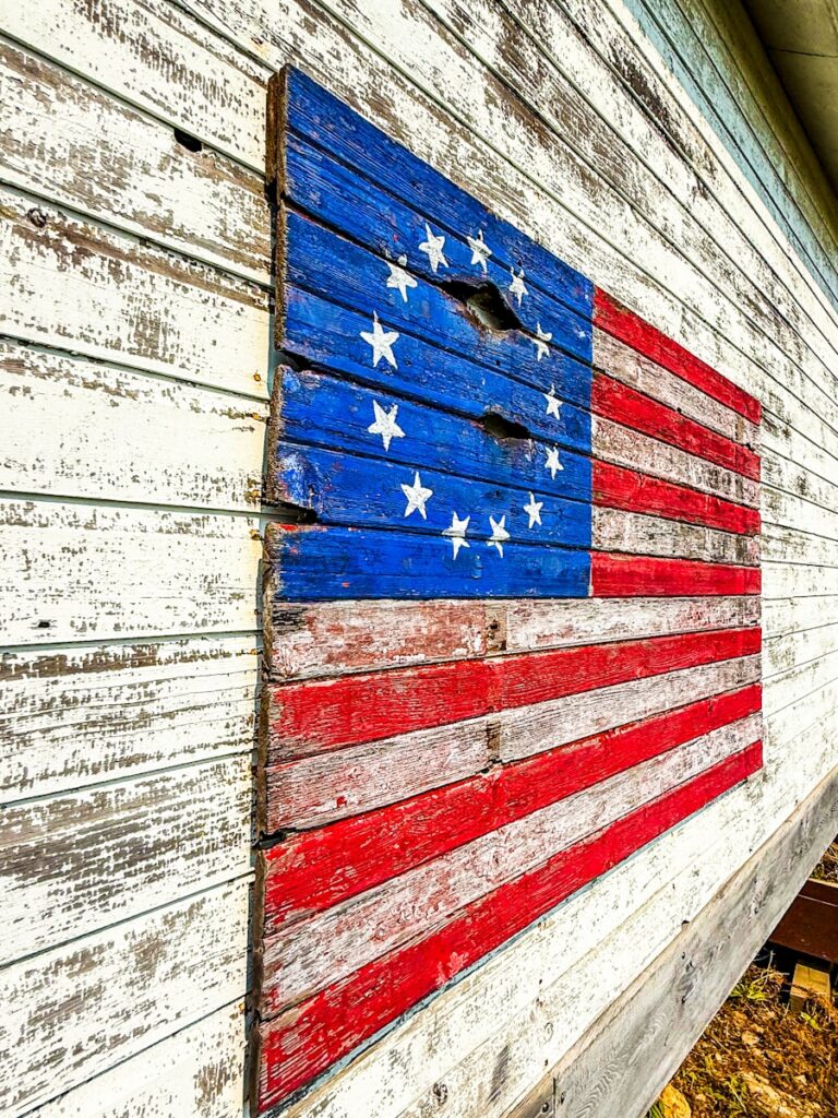 Rustic betsy ross flag mounted on weathered white wall.