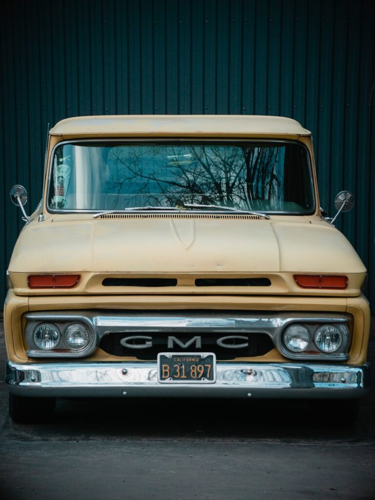 Here's a caption for the image: a yellow gmc truck is parked against a blue wall.