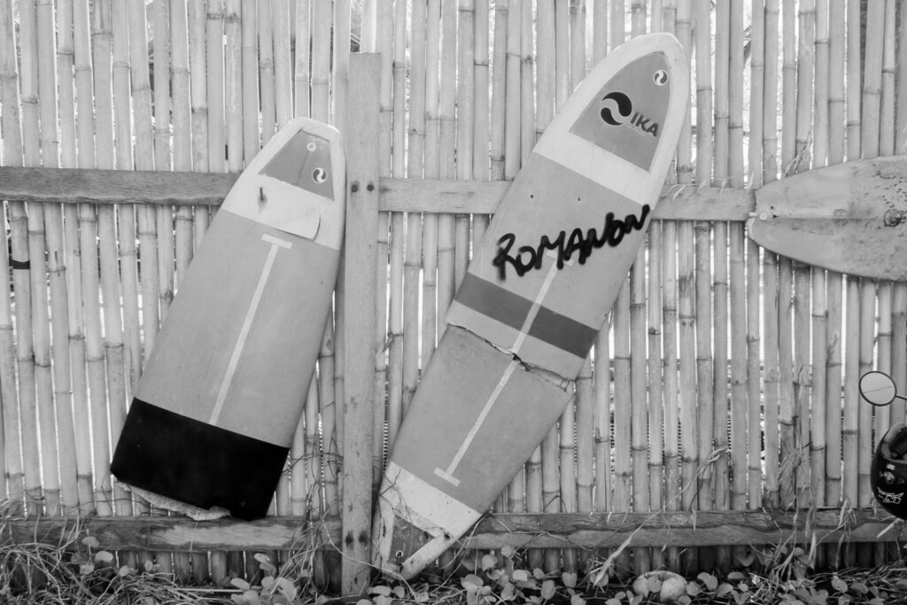 grayscale photo of two surfboard on wooden fence