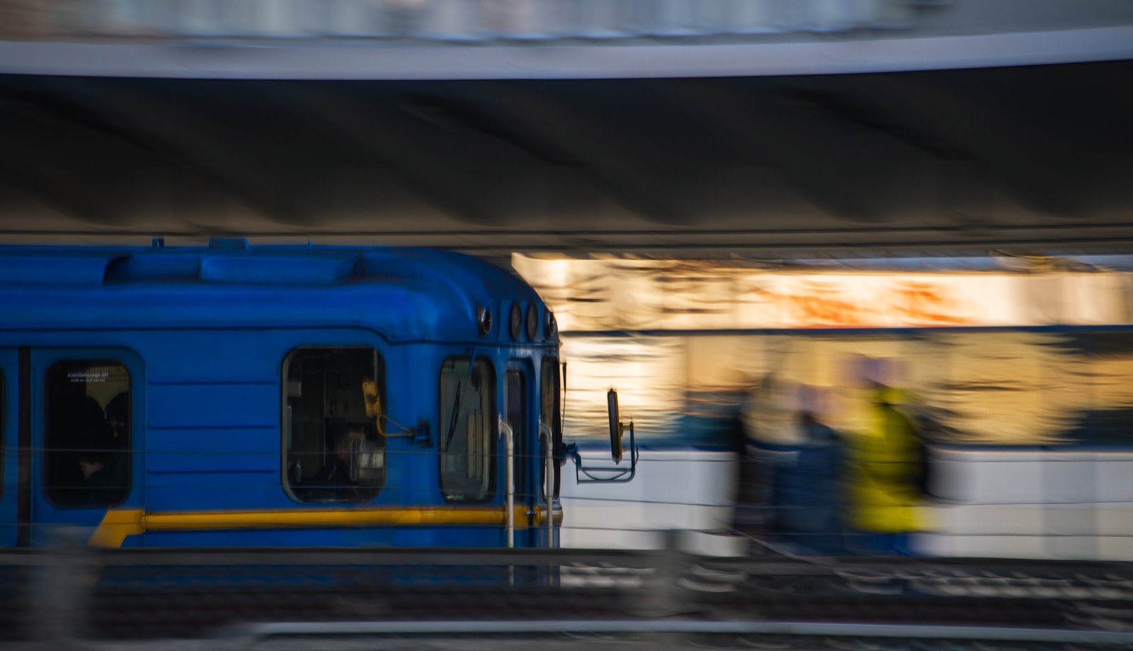 a blue train traveling down train tracks next to a loading platform