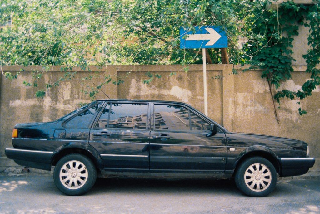 Black sedan parked on street with directional sign.