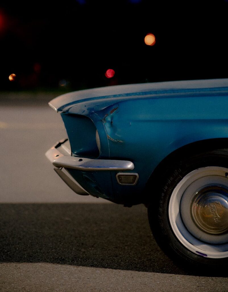 Close-up of a classic blue car with visible dents at night, showcasing vintage design and wear.
