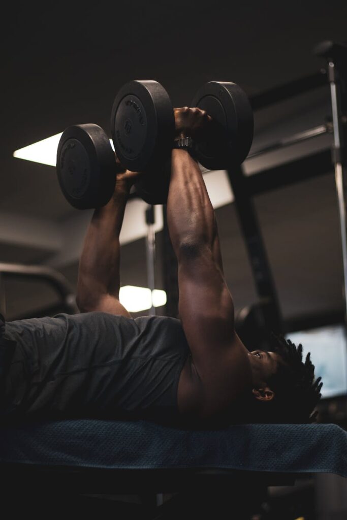 Adult male performing a dumbbell bench press in a gym setting.