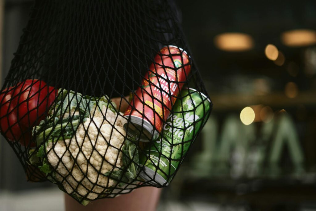 A mesh bag carrying fresh vegetables and canned drinks in an urban setting, showcasing eco-conscious shopping.
