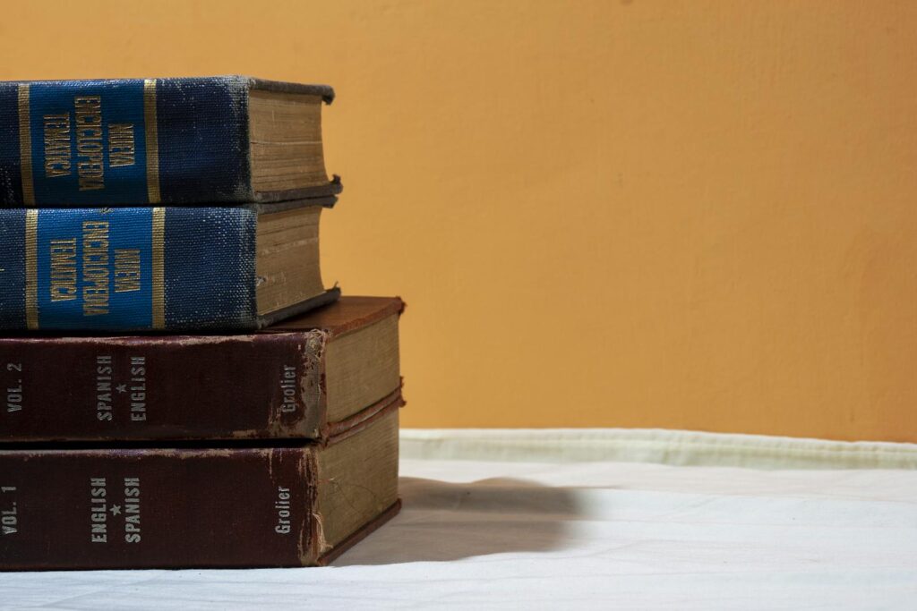A close-up of vintage English-Spanish dictionaries stacked on a table against a warm backdrop.