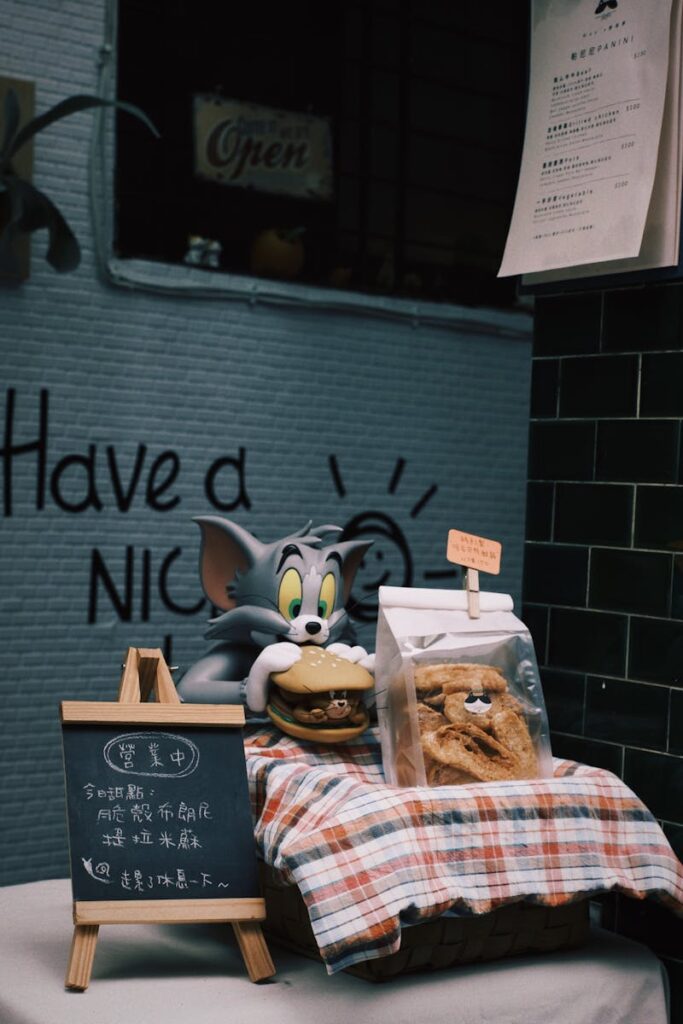 A playful Tom figurine holding a burger on a colorful table setting, next to a chalkboard menu.