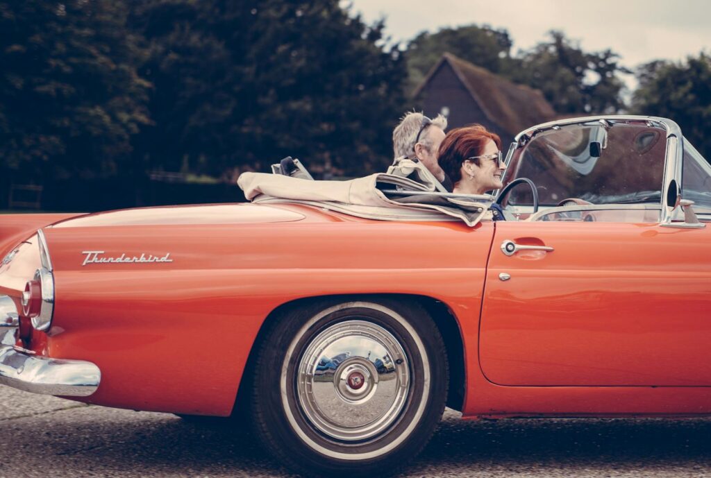 Smiling couple in a vintage red Thunderbird convertible enjoying a sunny drive outdoors.