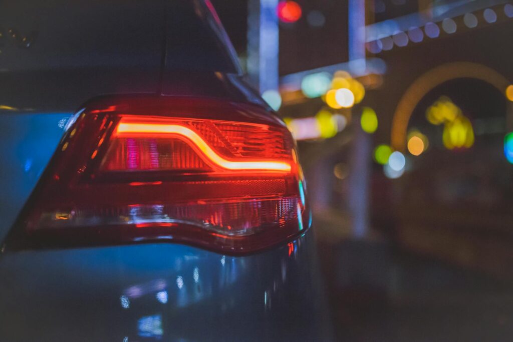 Close-up of a car's tail light with colorful bokeh background in an urban night setting.