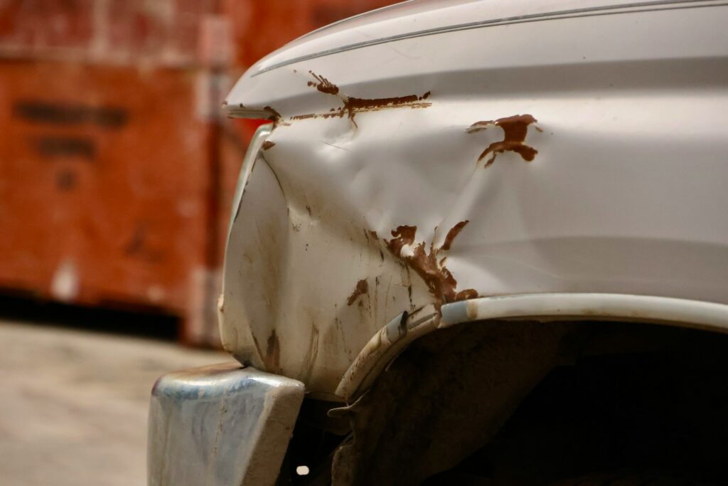 the front end of a white car with rust on it