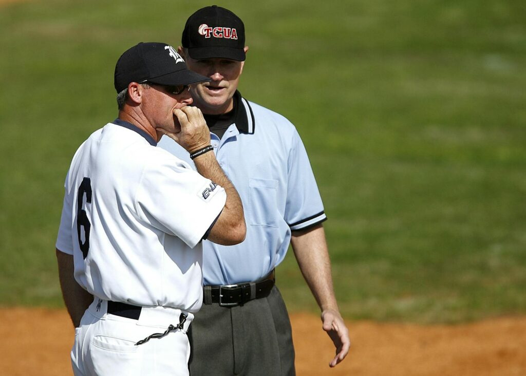 A baseball coach engages with an umpire on the field, discussing game strategy in uniform under a clear sky.