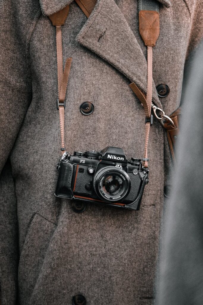Close-up of a vintage film camera hanging from a brown wool coat, showcasing classic photography equipment.