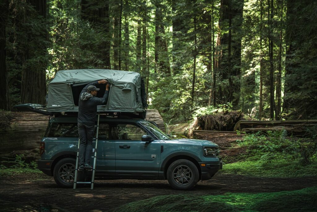 Person setting up rooftop tent on suv in forest.