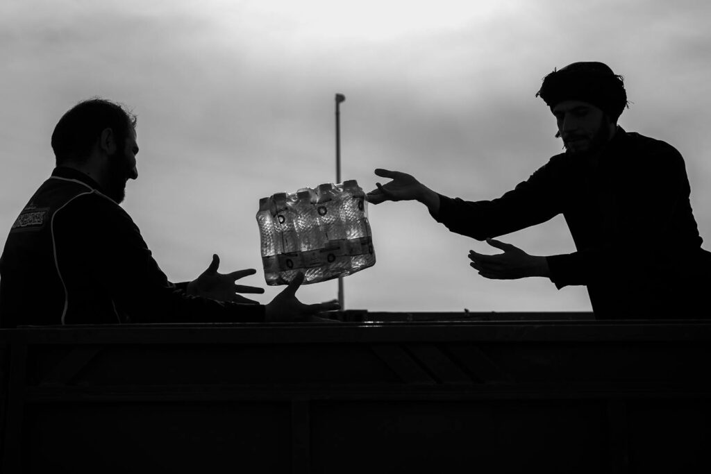 Silhouettes of two men exchanging bottled water in Mehran, Iran.