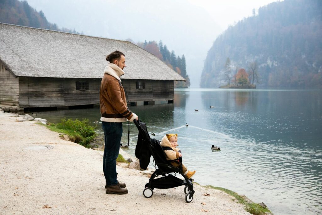 Father and child enjoy a peaceful stroll by the lake with ducks swimming nearby.
