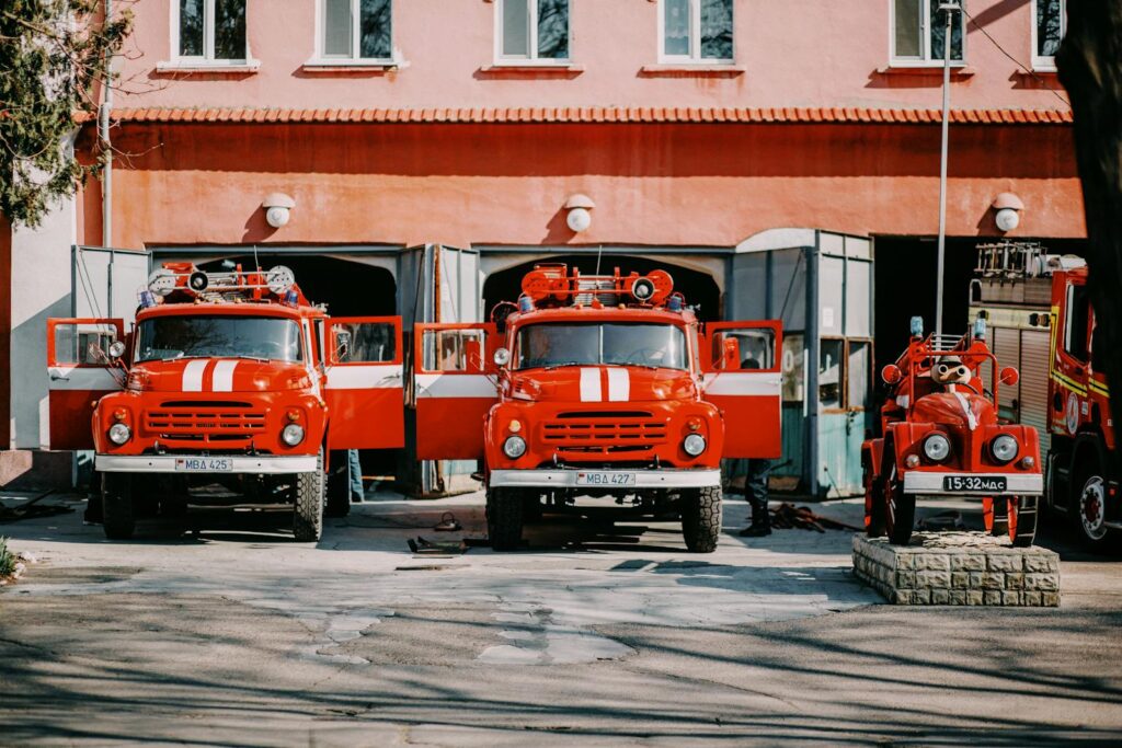 Front view of vintage red fire trucks parked side by side at a fire station outdoors.