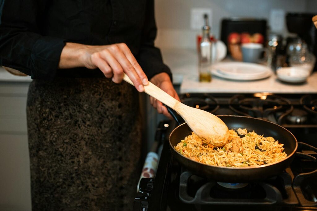 A woman stirs a delicious rice dish in a frying pan on a gas stove with a wooden spoon.