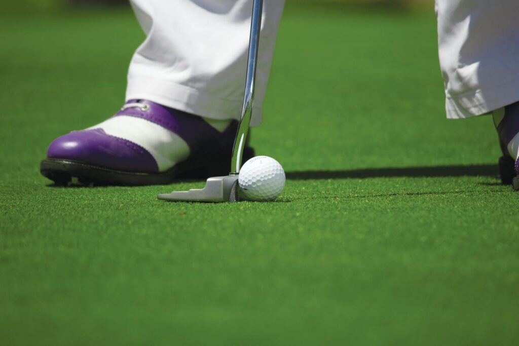 A golf player prepares to hit a ball with a putter on a green course.