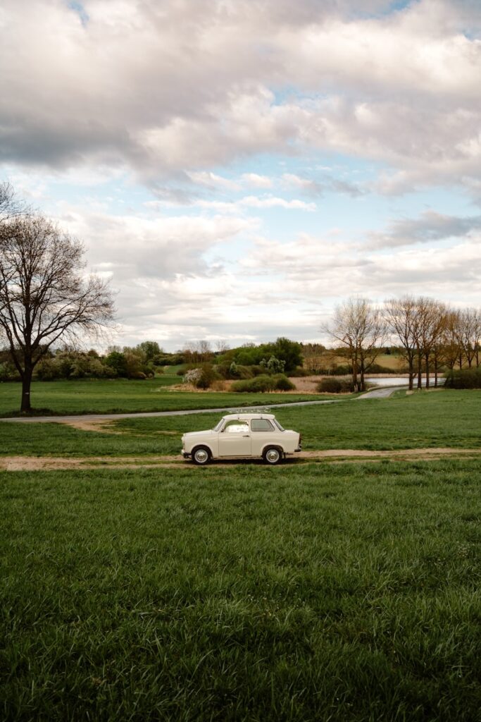 A classic car drives through a lush green field.