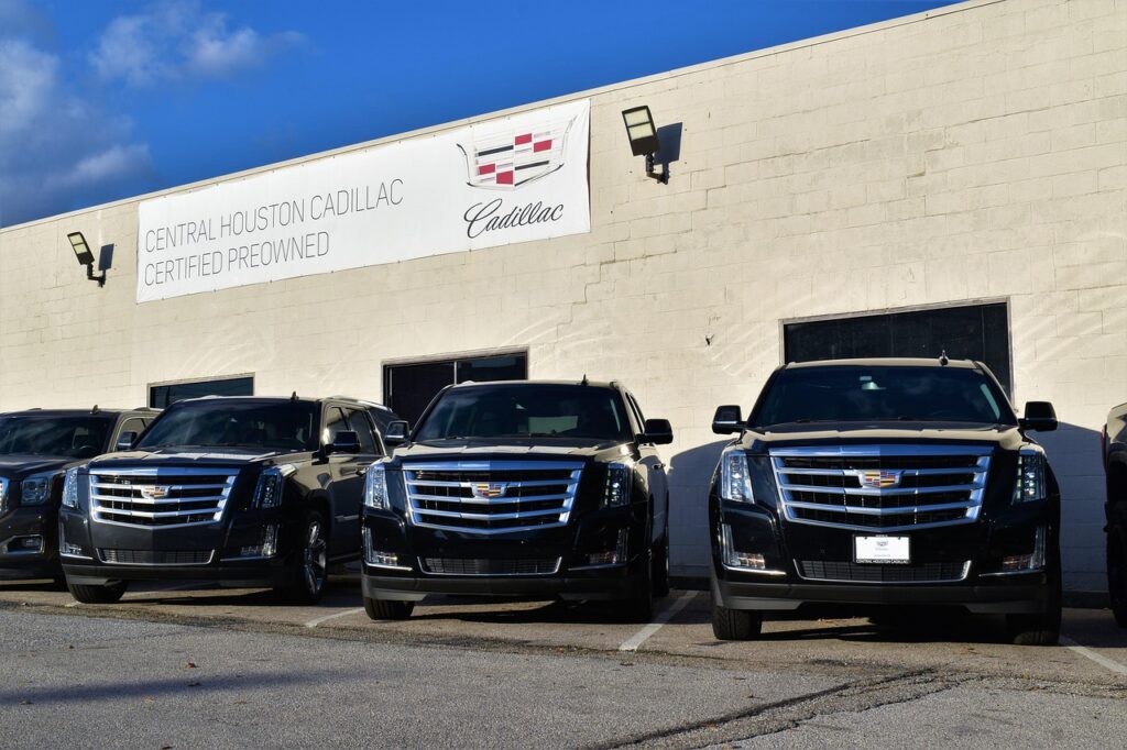 cadillac escalade suv, row of trucks, long wheel base, sport edition, black, security vehicles, bumper, logo, facing camera, front exterior, building, banner, security lights, night light, headlight, daytime running lights, used cars, pre-owned, insurance, investing, depreciation, range rover, competition, direct sales floor, chrome grill, depreciation, depreciation, depreciation, depreciation, depreciation
