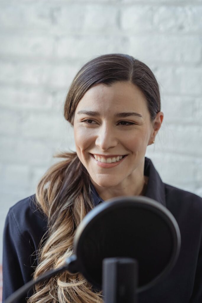 Cheerful woman speaking into a microphone, recording a podcast indoors.