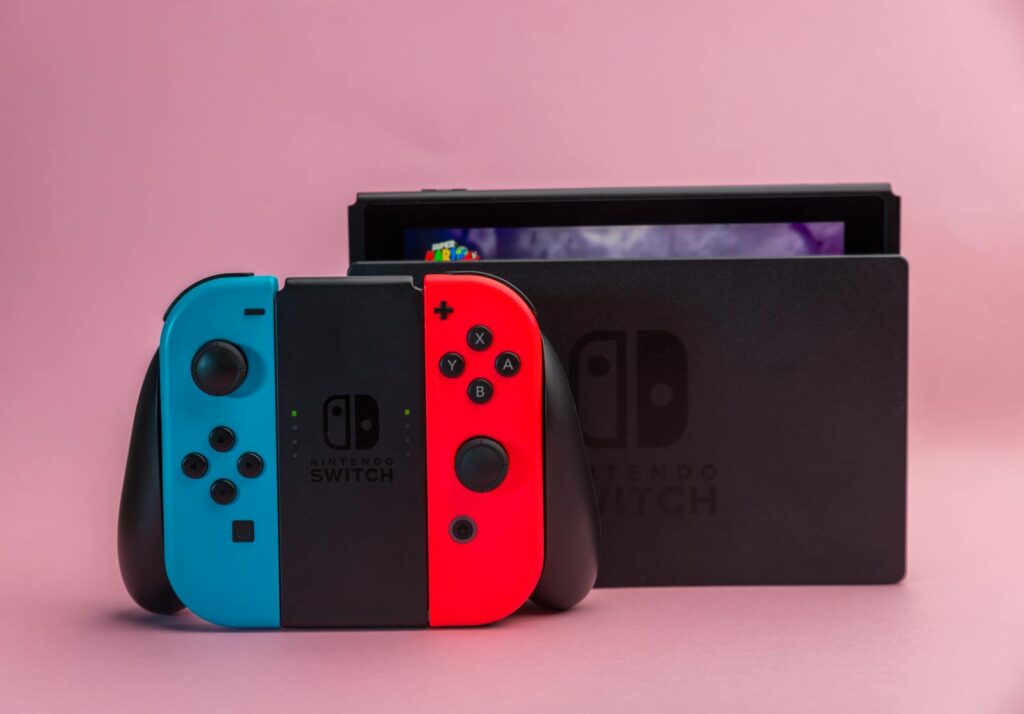 Close-up of Nintendo Switch console with red and blue Joy-Con controllers on pink background.