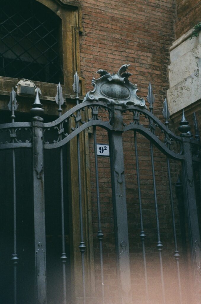 an iron gate with a clock on it in front of a brick building