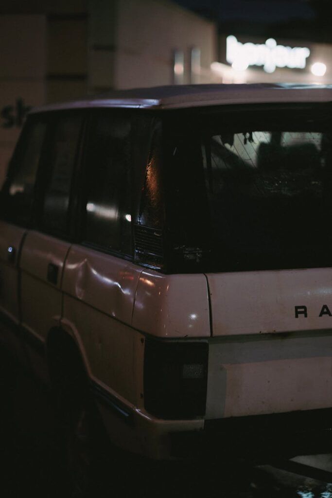 Classic white SUV with visible damage parked in a dimly lit urban area at night.