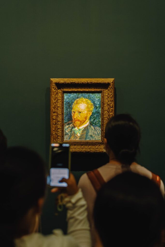 People viewing a van gogh self-portrait in a museum.