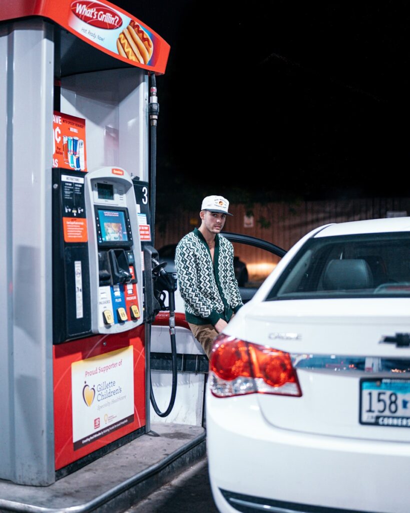 a man sitting at a gas pump next to a white car