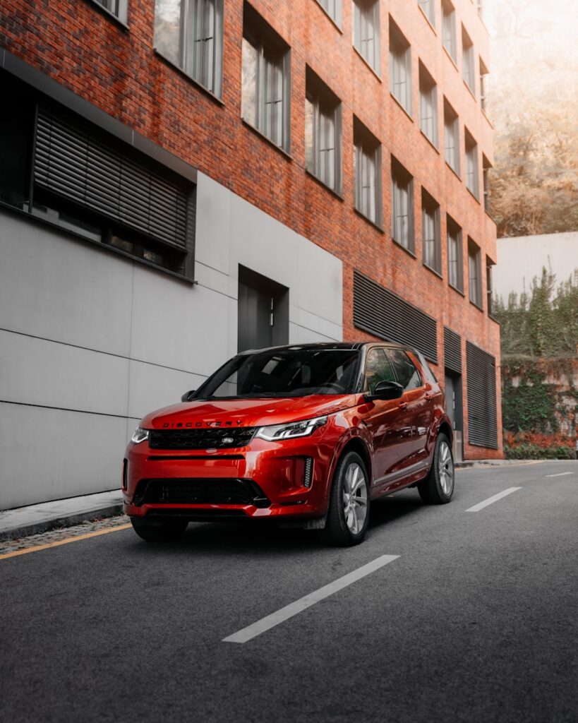 red car parked beside white concrete building during daytime