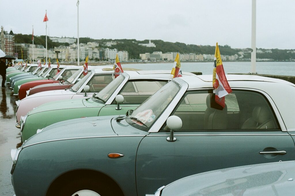 Line of vintage cars with flags on a waterfront.