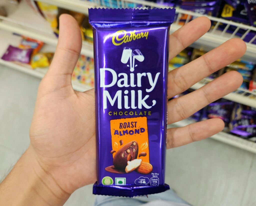 A hand holds a cadbury dairy milk roast almond chocolate bar.
