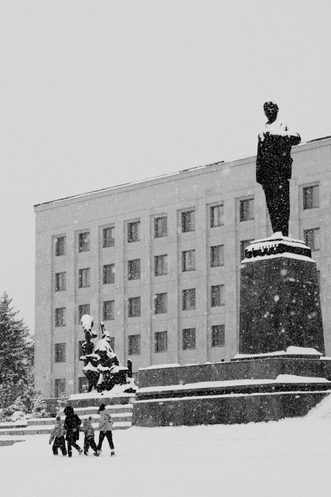 a black and white photo of people walking in the snow in front of a building
