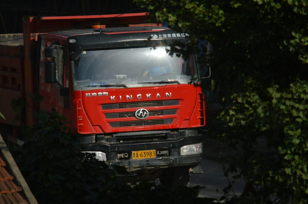 A red truck driving down a road next to a forest