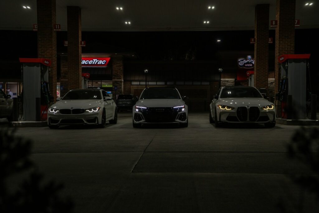 Three cars are parked at a gas station at night.