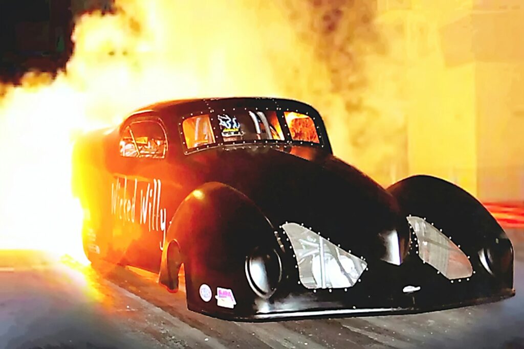 Black drag racing car with flames erupting from exhaust.