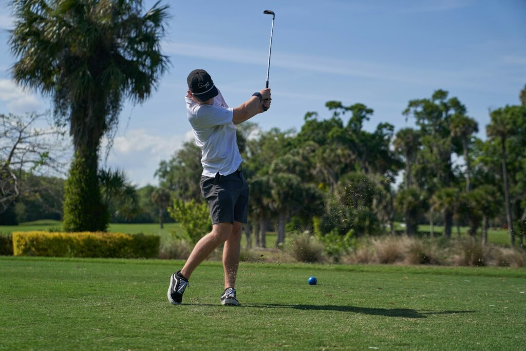man in white shirt and black shorts playing golf during daytime