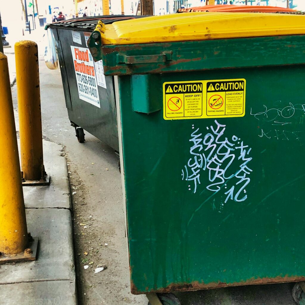 a green trash can sitting on the side of a road